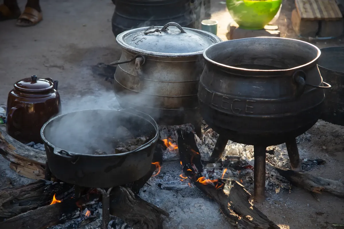 Traditional outdoor cooking with cast iron pots and open fire.