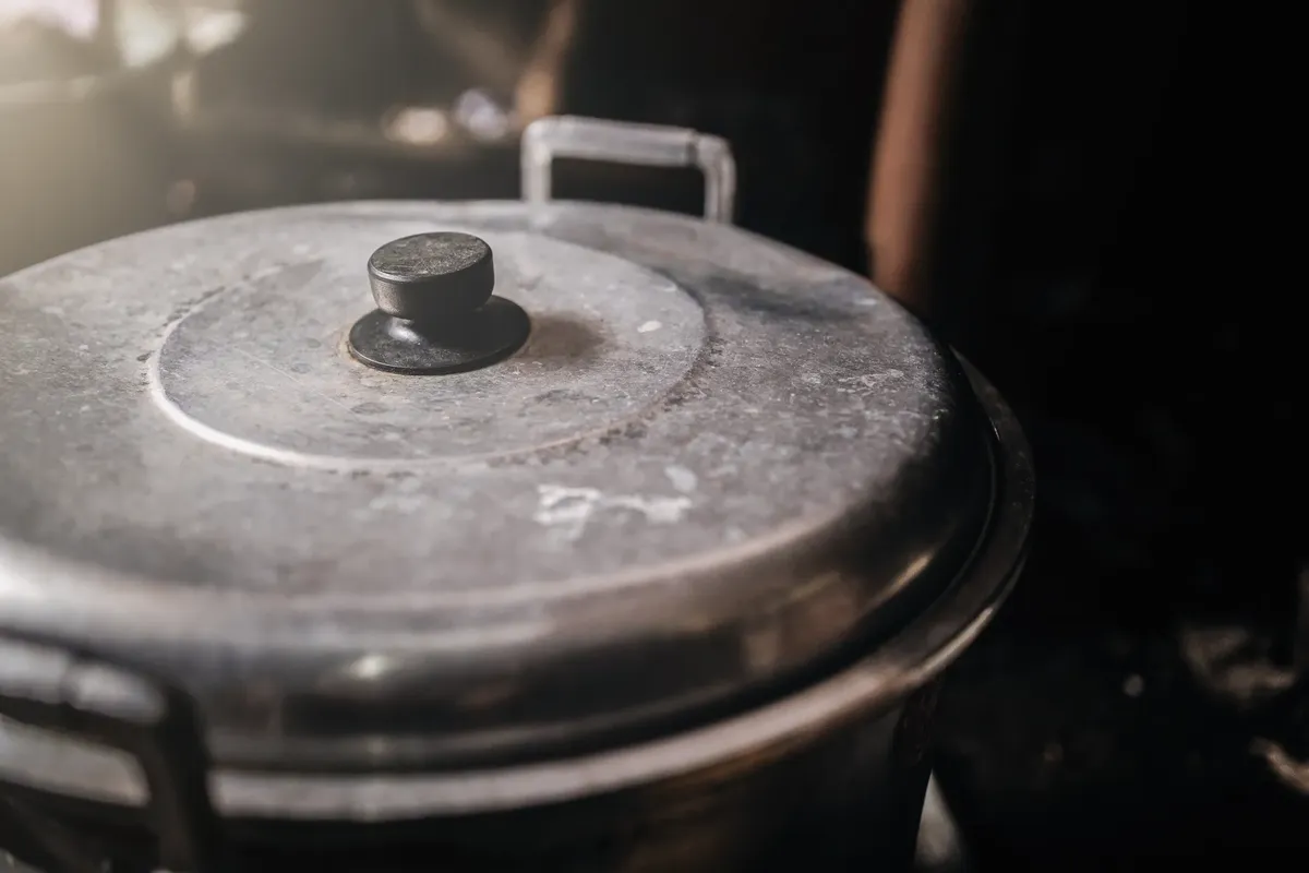 Detailed view of an old metal cooking pot with a black handle in a rustic kitchen setting.