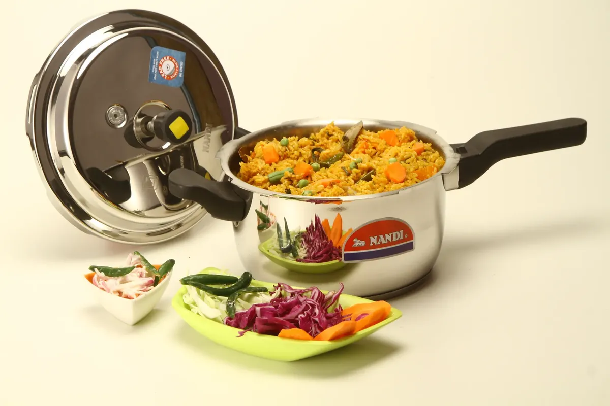 Colorful vegetable biryani cooked in a stainless steel pressure cooker with fresh ingredients.