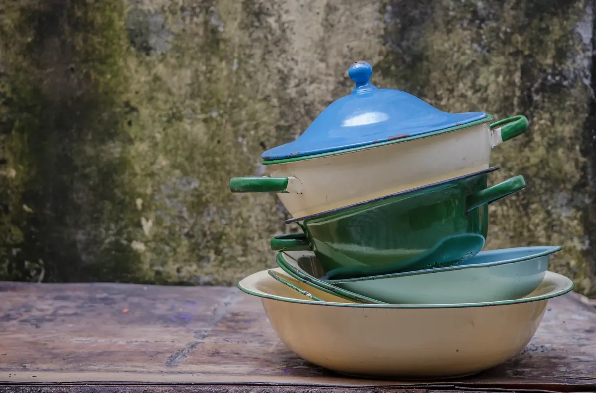 A rustic stack of colorful vintage enamel pots and pans outdoors against a textured wall.