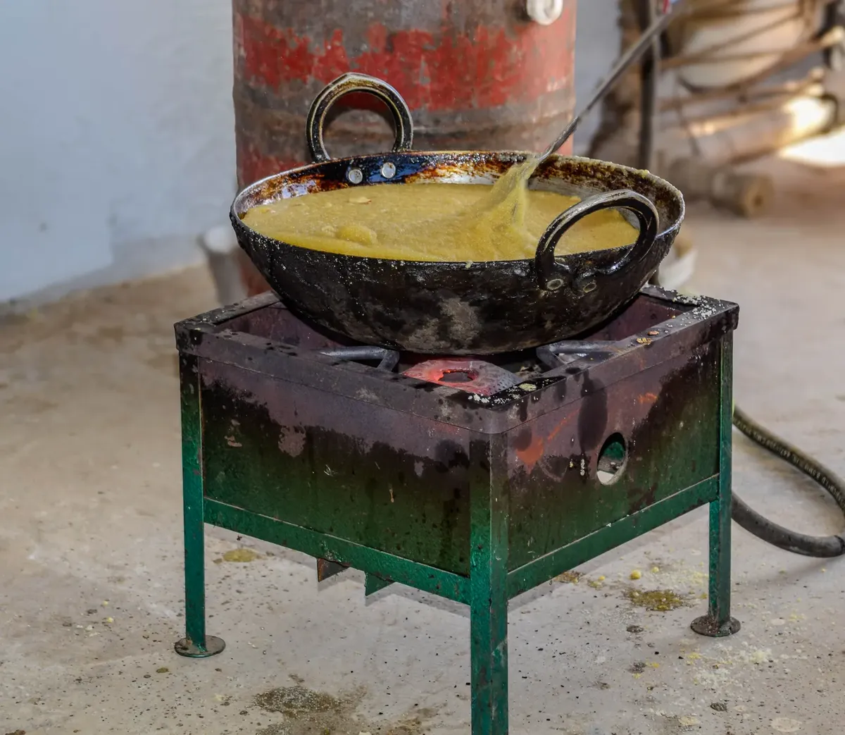 Traditional dish being prepared in a cast iron kadai on a rustic stove.